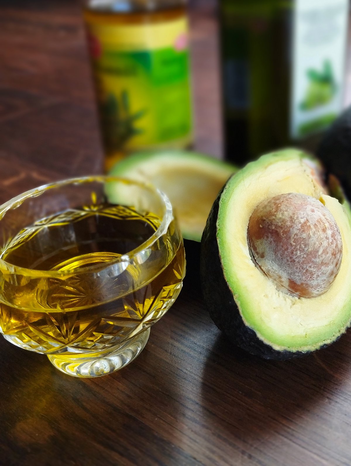 A small glass of olive oil sits beside an avocado cut in half.