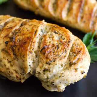 A grilled lemon herb chicken breast sits on a plate