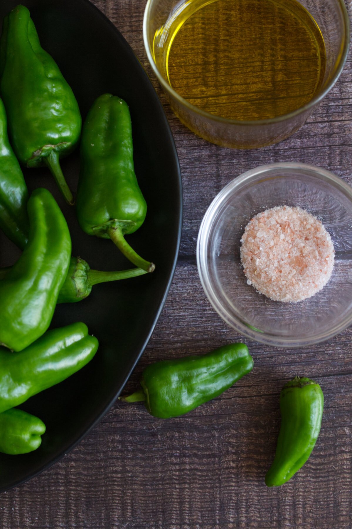 Some uncooked pardon peppers sit beside some olive oil and salt