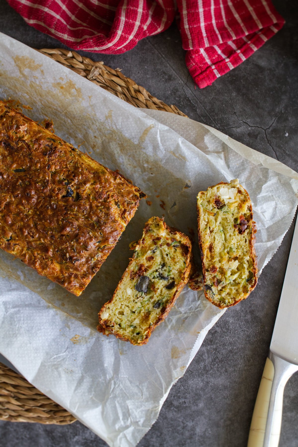 A mediterranean zucchini bread sits sliced on a cutting board. 