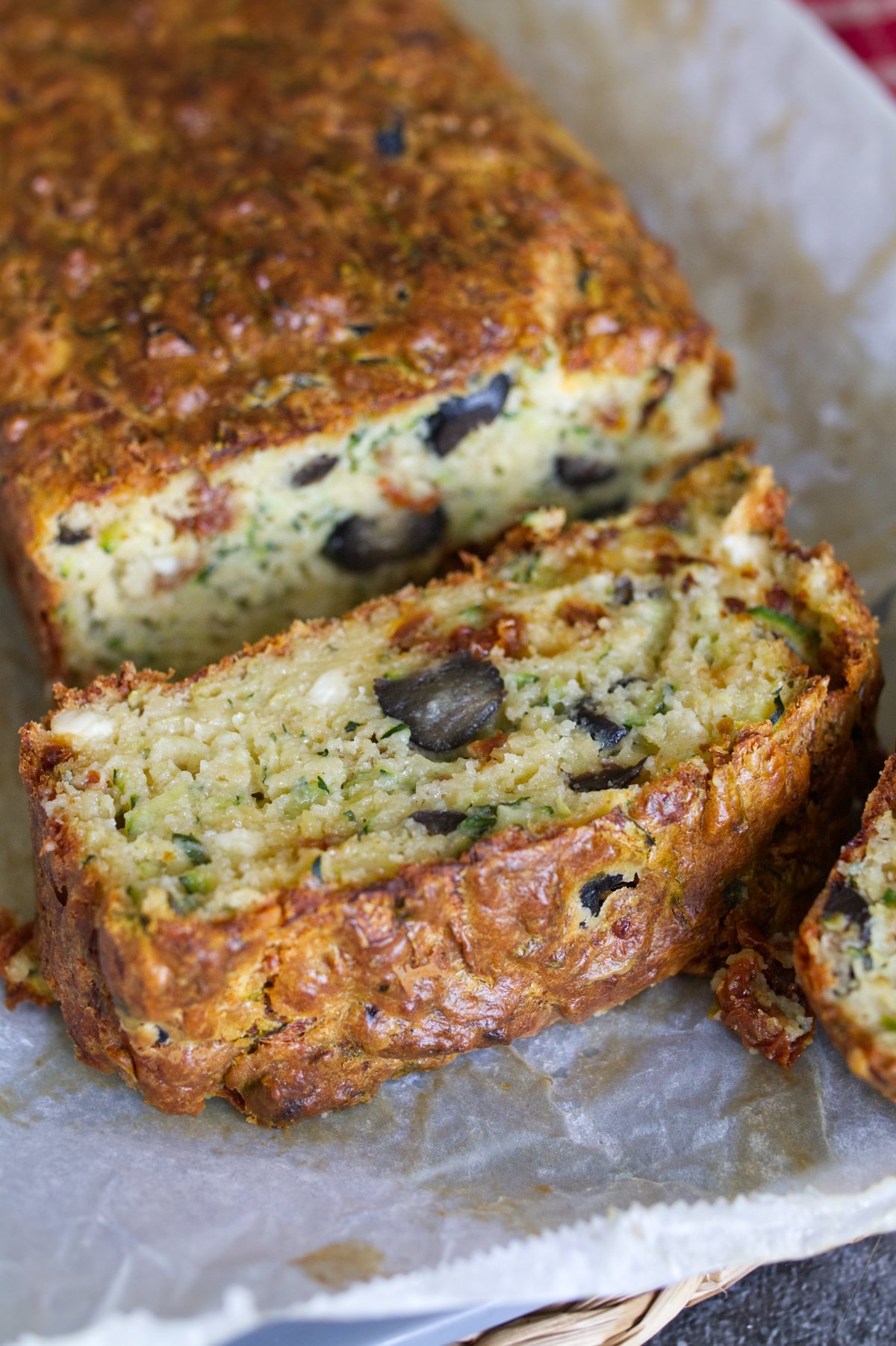 A mediterranean zucchini bread sits sliced on a cutting board.