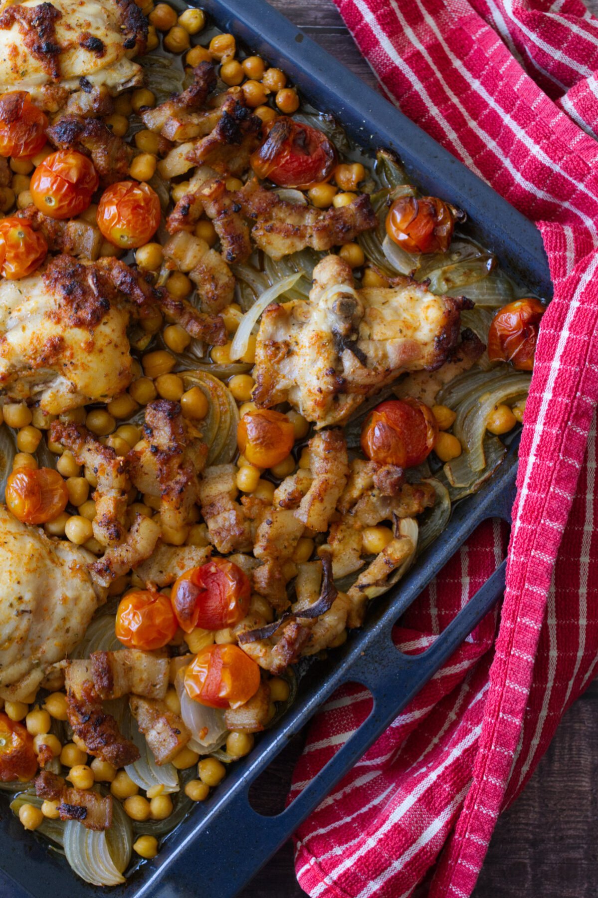 A large sheet pan of baked Mediterranean chicken thighs with chickpeas and pancetta