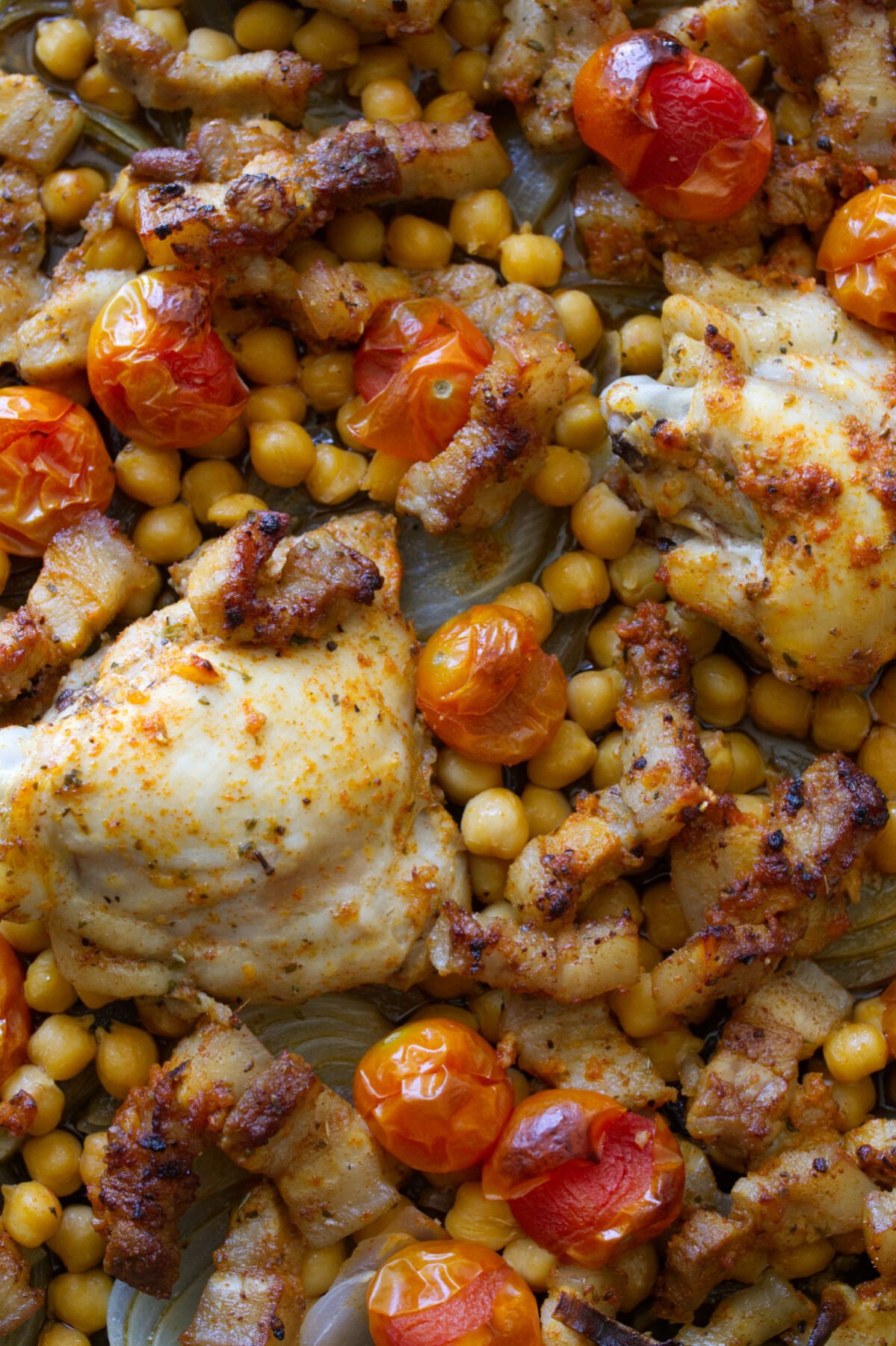 A large sheet pan of baked Mediterranean chicken thighs with chickpeas and pancetta