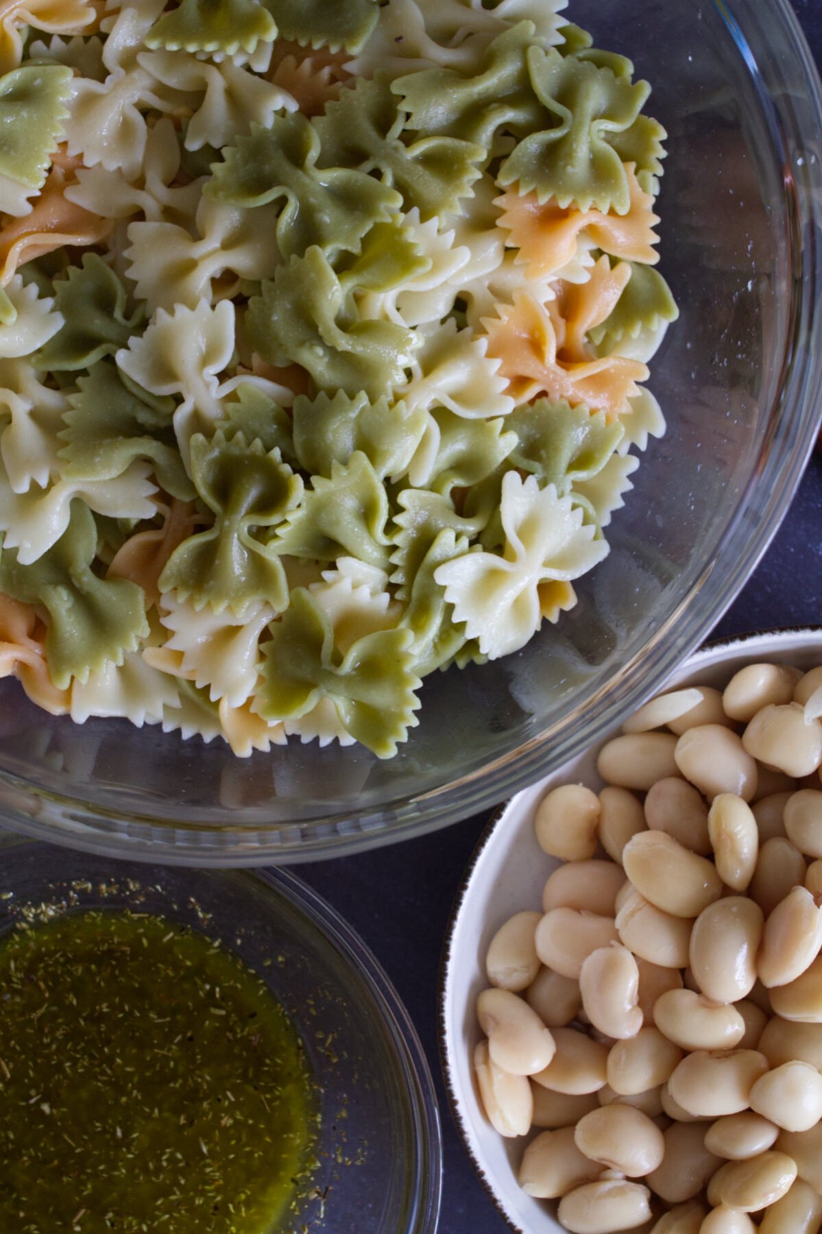 Some farfalle pasta sits beside some white beans