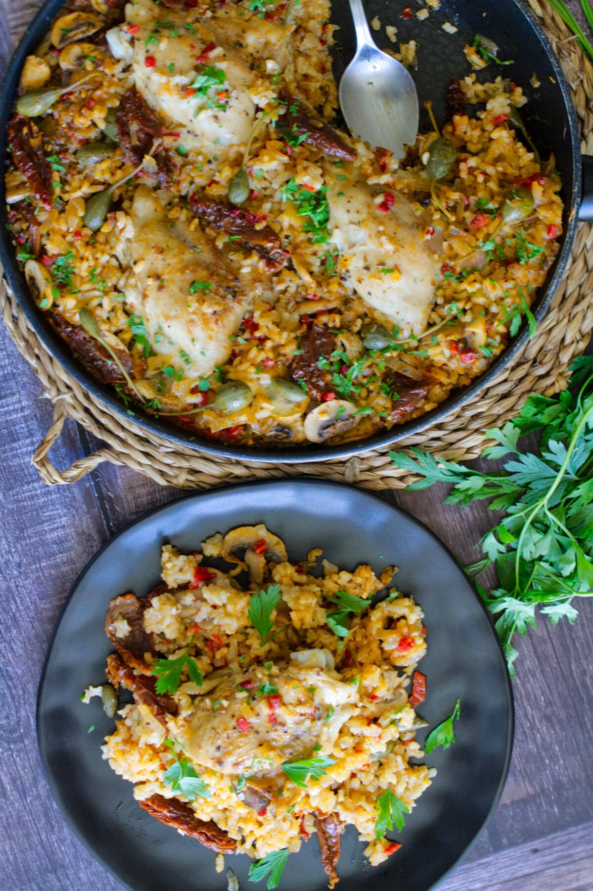 A large pan of Italian Chicken thighs with lots of rice sits beside a serving plate