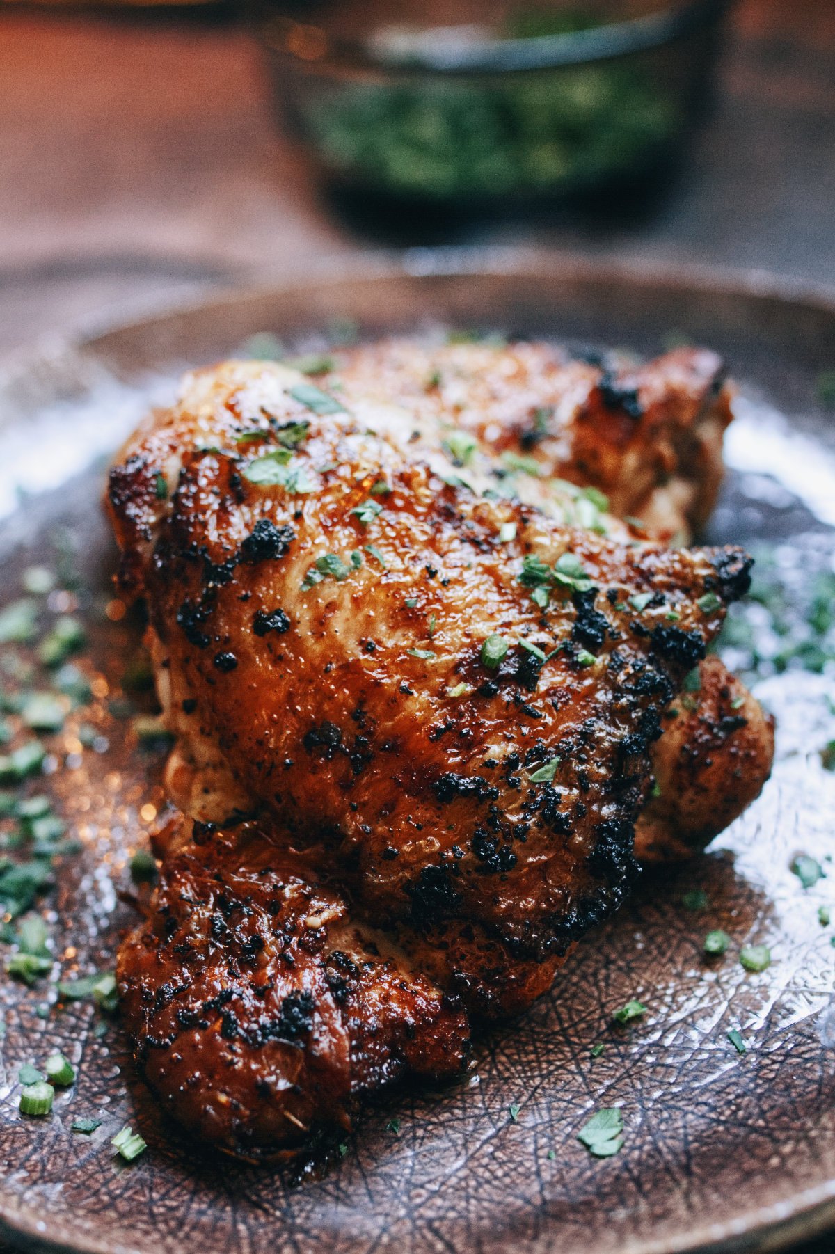 A spicy paprika chicken thigh sits on a plate with some parsley as garnish