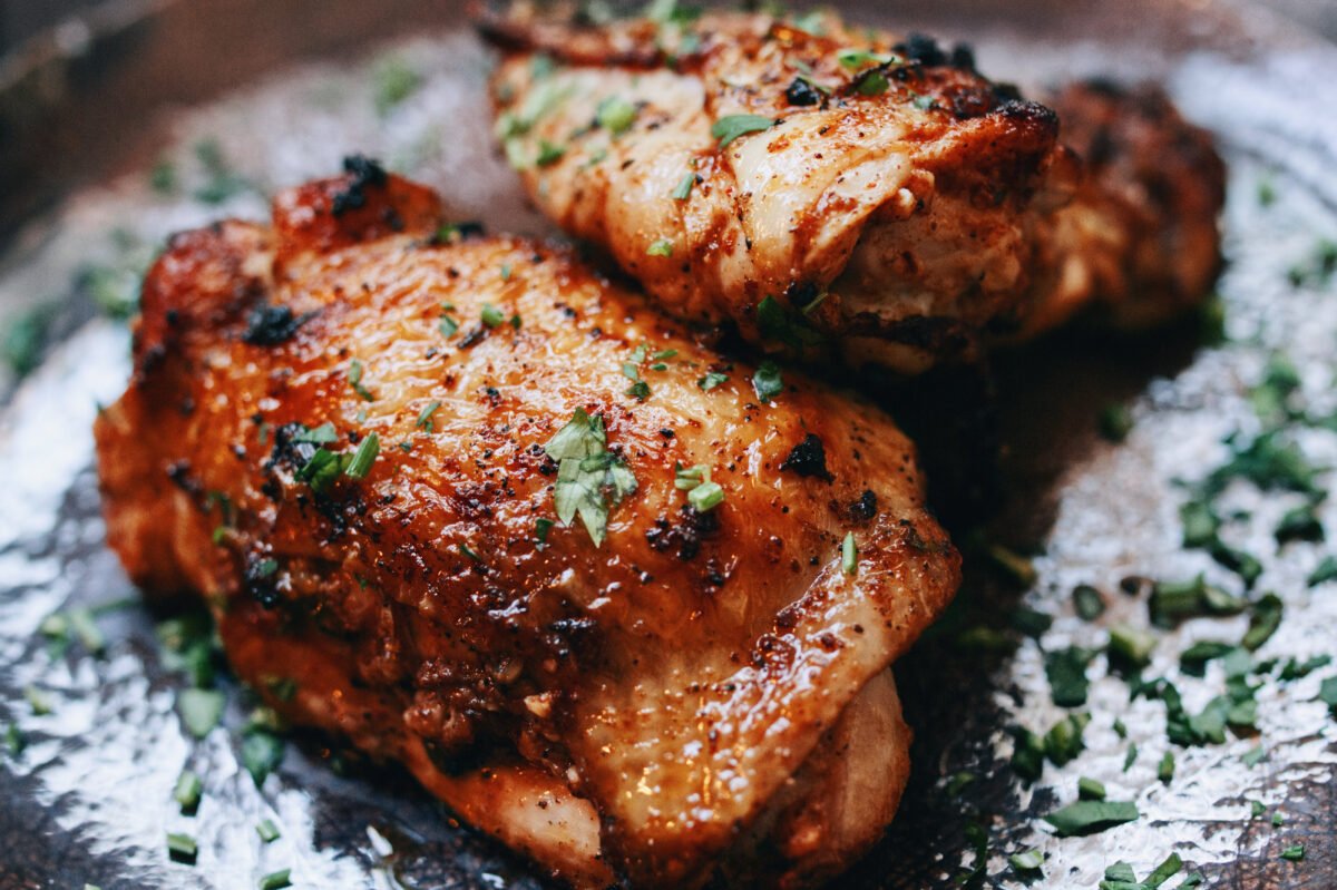 A spicy paprika chicken thigh sits on a plate with some parsley as garnish