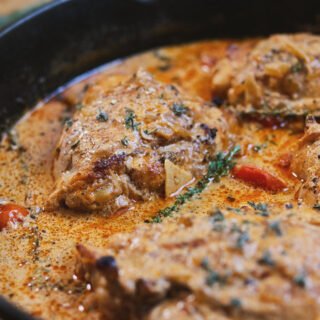 A skillet of creamy Mediterranean chicken thighs garnished with fresh thyme