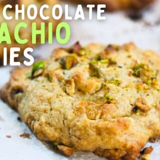 A white chocolate pistachio cookie sits on a baking rack waiting to cool.