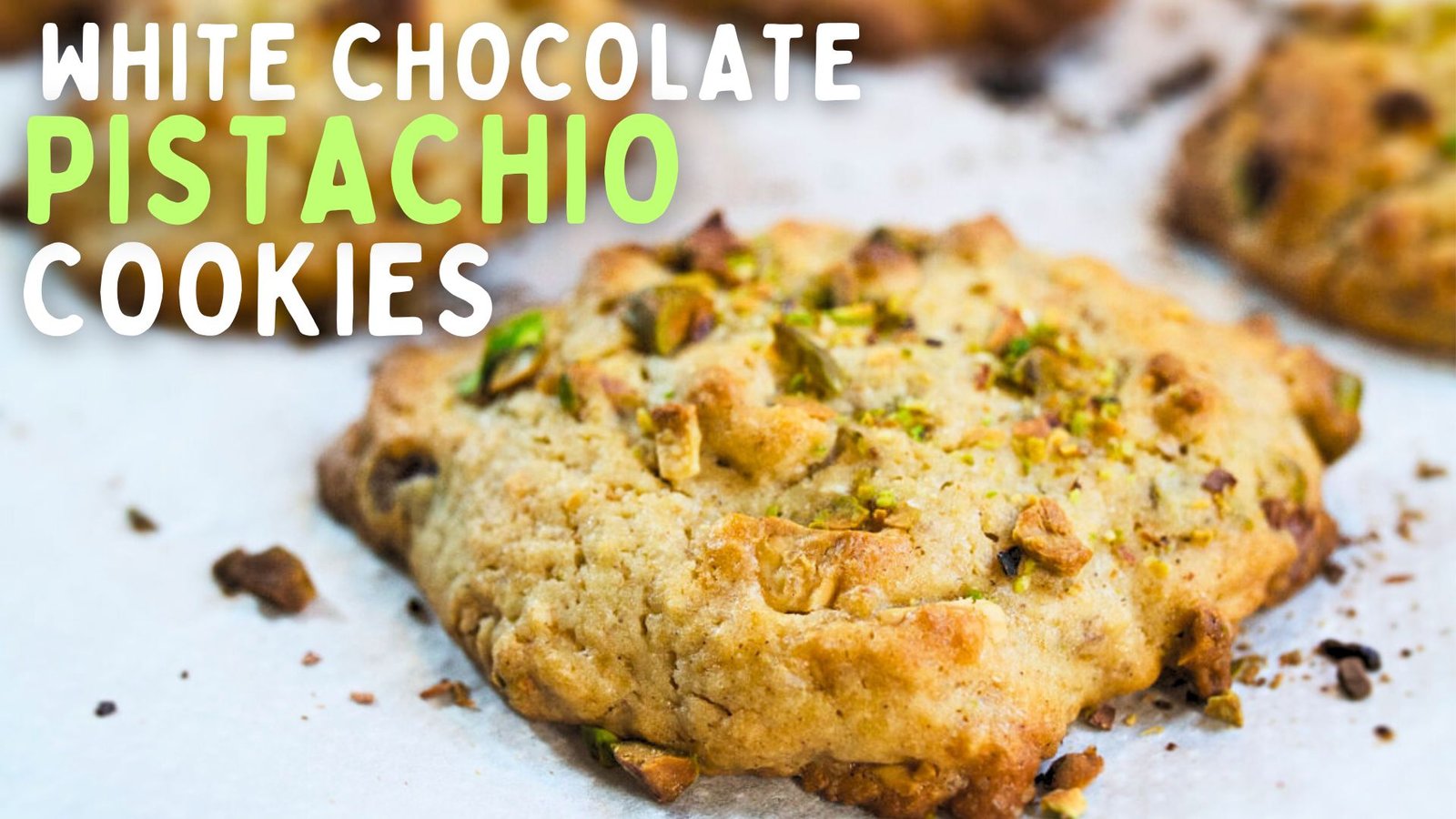 A white chocolate pistachio cookie sits on a baking rack waiting to cool.