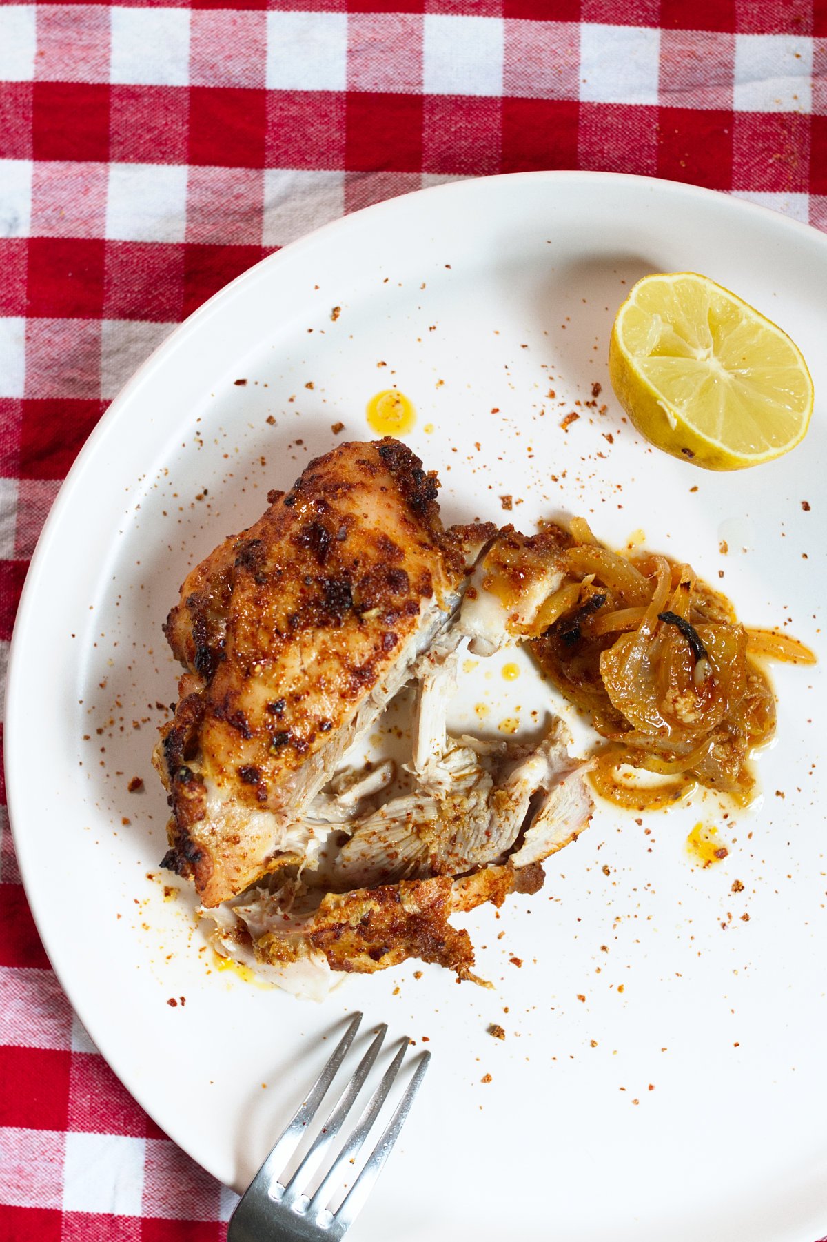 A plate with a spicy Mediterranean chicken thigh served with some lemon