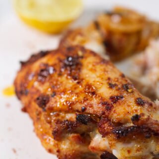 A plate with a spicy Mediterranean chicken thigh served with some lemon