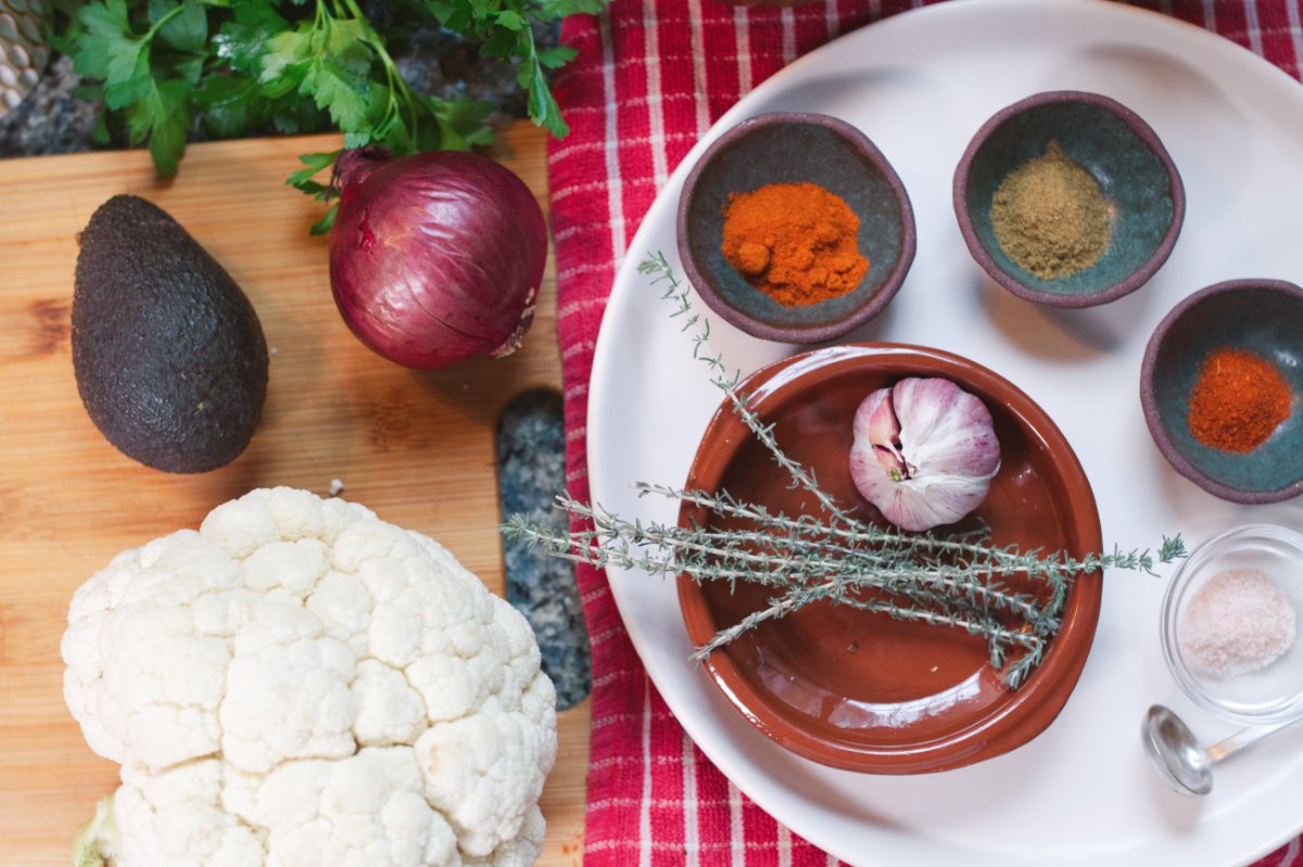 A cauliflower and some spices sit on a cutting board