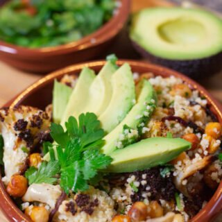 A bowl of Spicy roasted cauliflower & chickpeas sits garnished with some sliced avocado