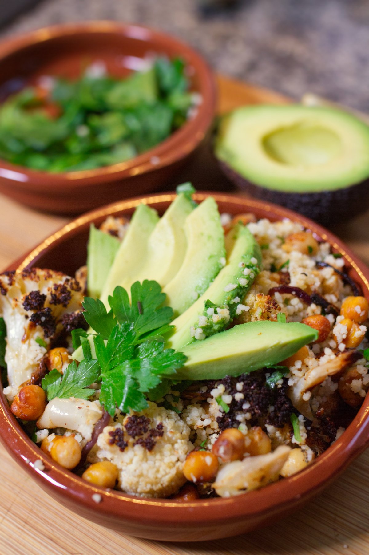 A bowl of Spicy roasted cauliflower & chickpeas sits garnished with some sliced avocado