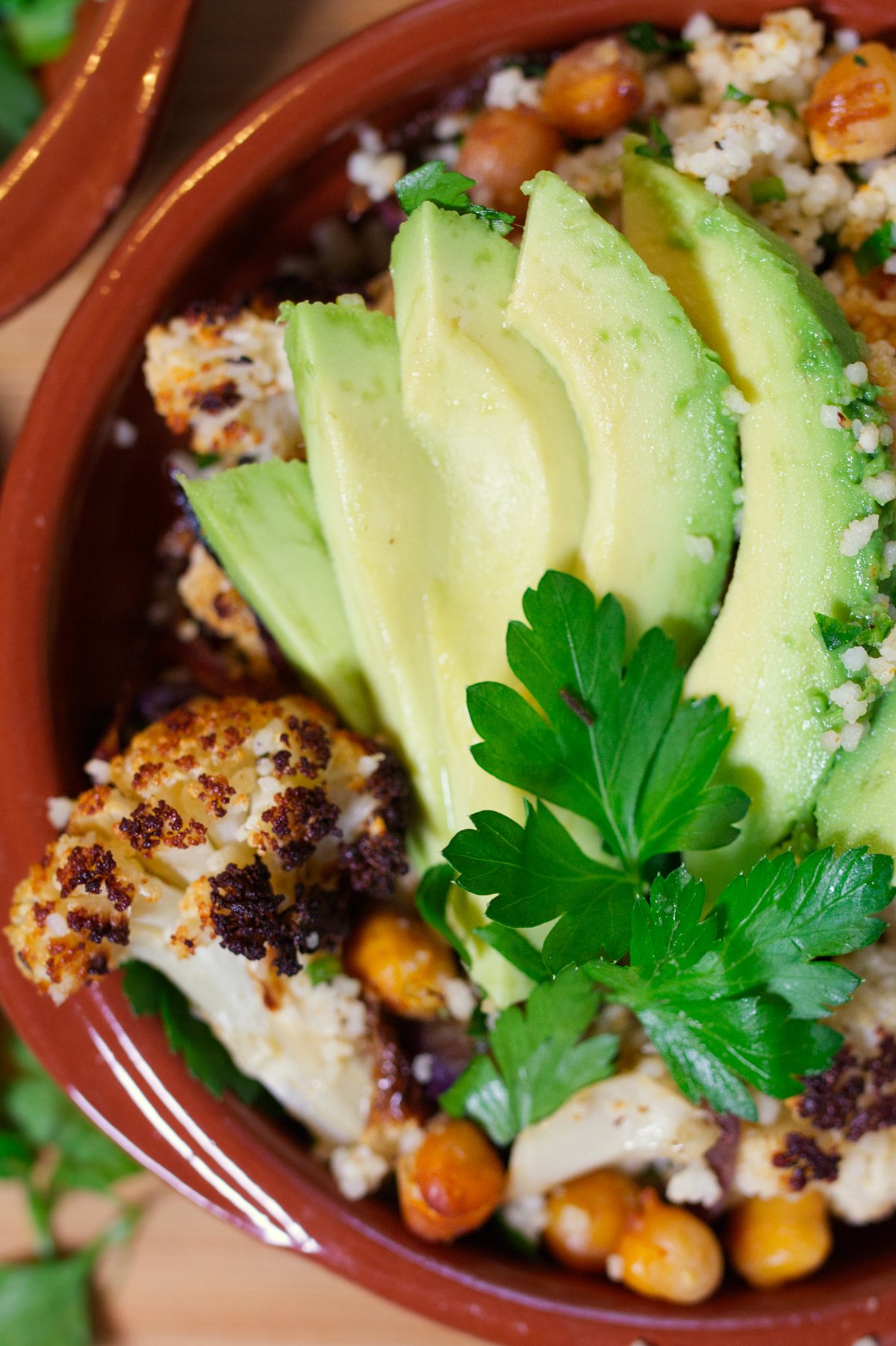 A bowl of Spicy roasted cauliflower & chickpeas sits garnished with some sliced avocado