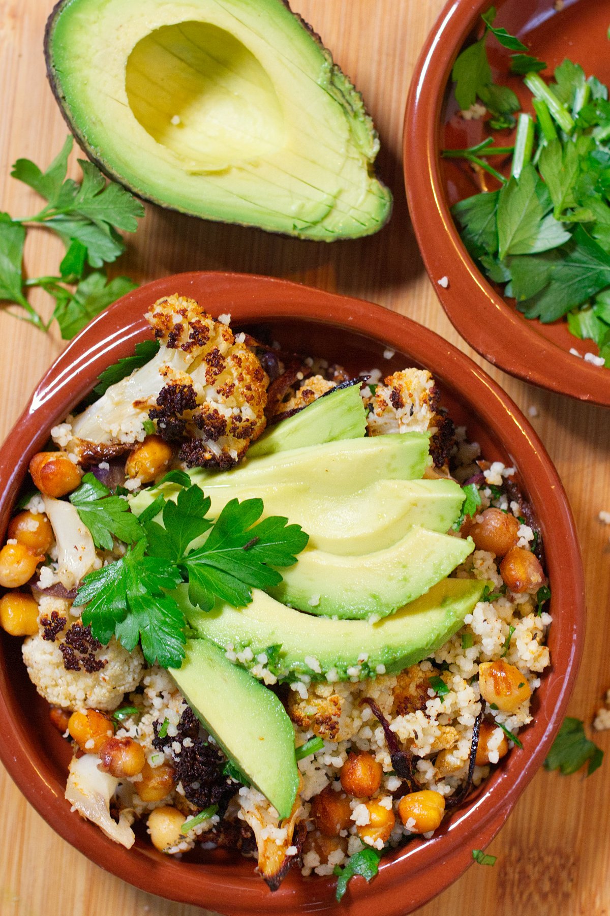 A bowl of Spicy roasted cauliflower & chickpeas sits garnished with some sliced avocado