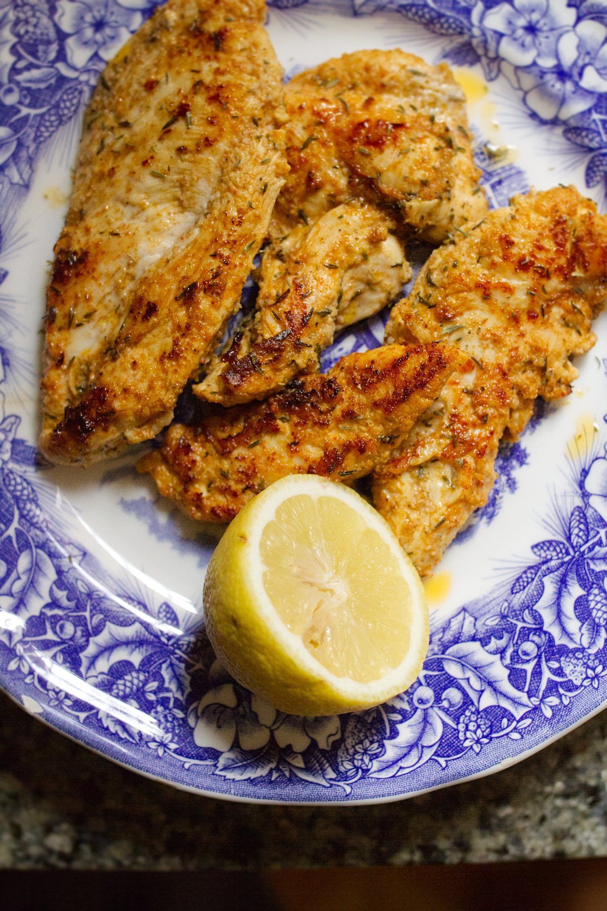 A plate of marinated chicken breasts with a wedge of lemon