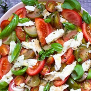 A large platter of tomato mozzarella salad garnished with fresh basil leaves