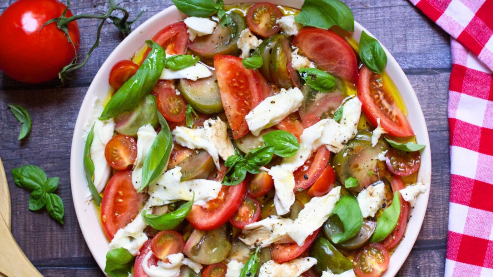 A large platter of tomato mozzarella salad garnished with fresh basil leaves