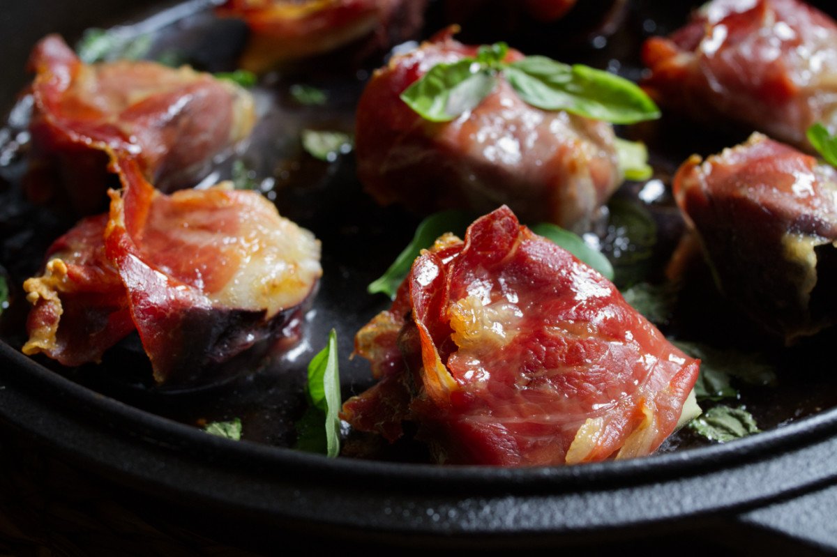 A skillet with cooked figs in a blanket of Serrano ham