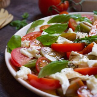 tomato mozzarella salad-v19 - happymediterranean.com A large platter of tomato mozzarella salad garnished with fresh basil leaves