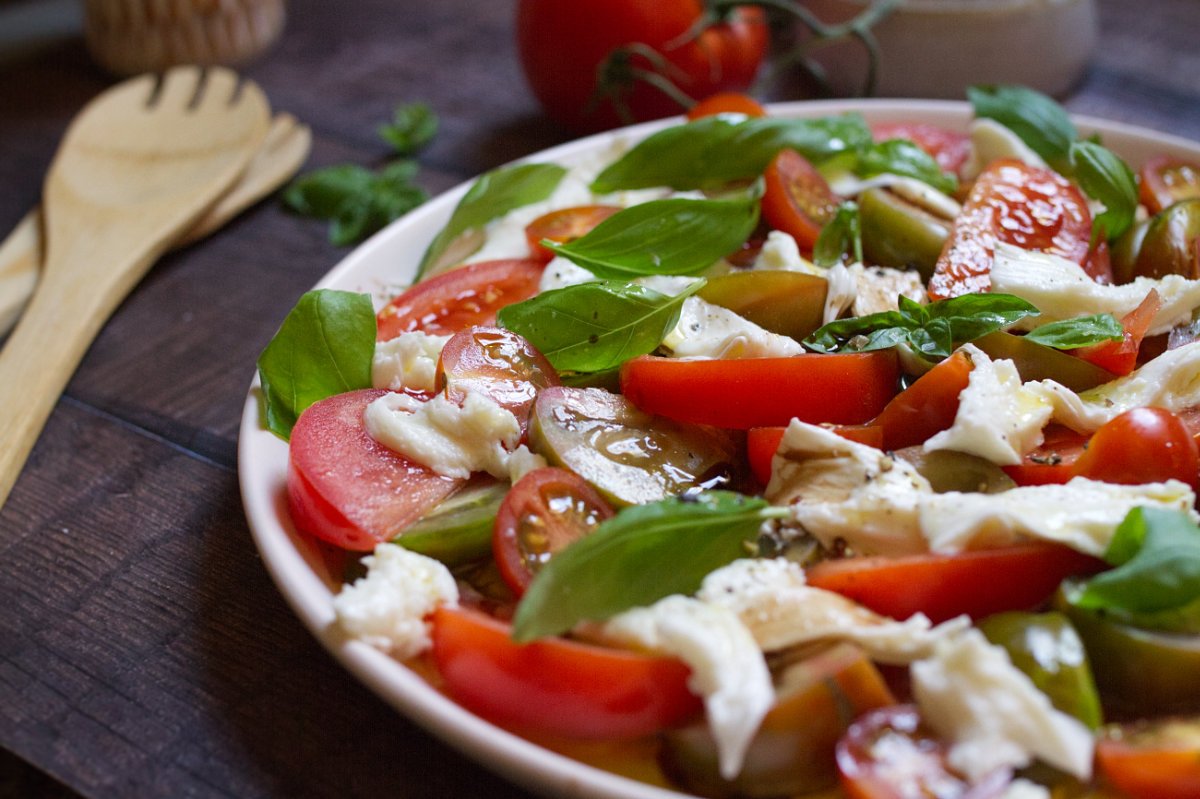 tomato mozzarella salad-v19 - happymediterranean.com A large platter of tomato mozzarella salad garnished with fresh basil leaves