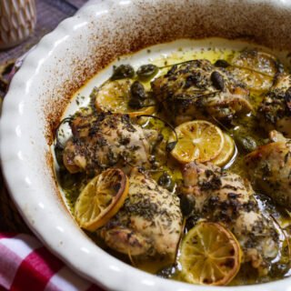 A large dish of Greek lemon and herb chicken thighs sits waiting to be served