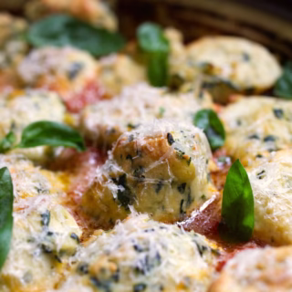 A pan of Malfatti Italian spinach and ricotta dumplings in a pan with basil and parmesan cheese