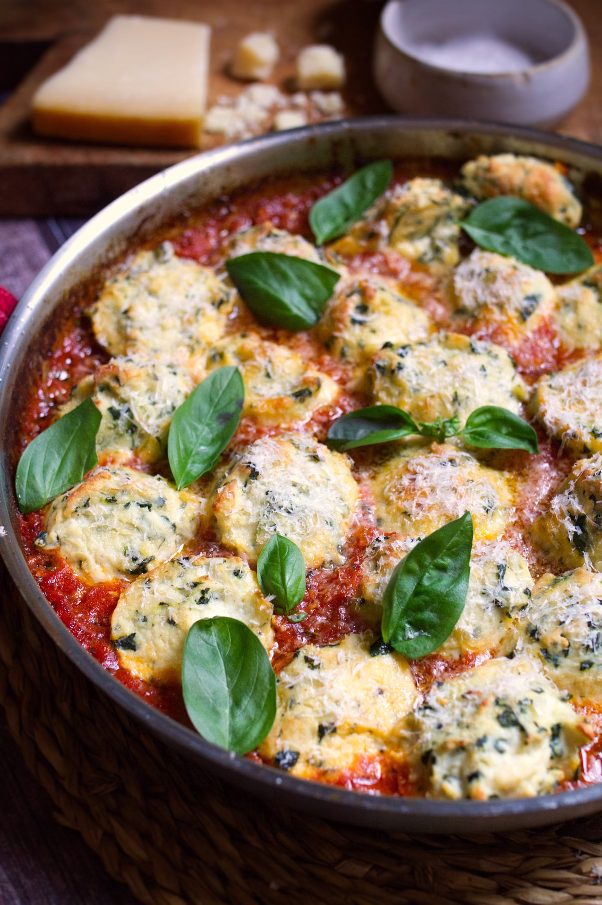 A pan of Malfatti Italian spinach and ricotta dumplings in a pan with basil and parmesan cheese