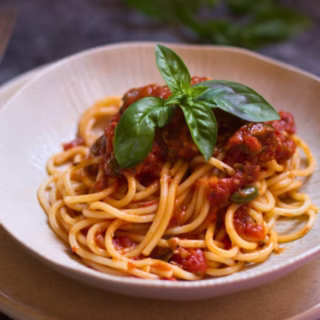 A serving of Spaghetti Puttanesca with some basil for garnish