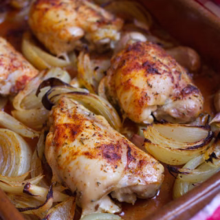 Mediterranean chicken thighs-v17 - happymediterranean.com a pan of chicken thighs with cooked onion and garlic
