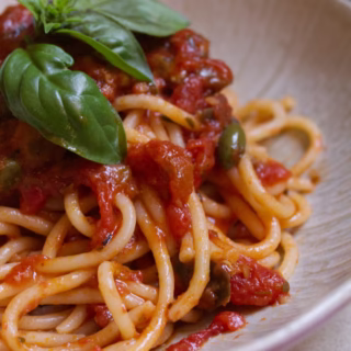 Spaghetti-puttanesca-v9 - happymediterranean.com A serving of Spaghetti Puttanesca with some basil for garnish